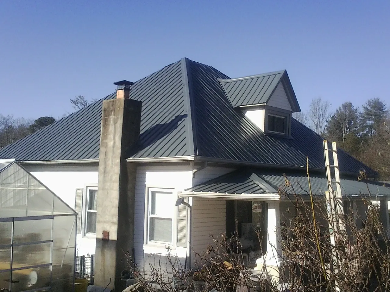 Dark blue standing seam metal roof on a white farmhouse with dormer — Slate & Tile Roof Repair by Roofing Brothers in King Hill
