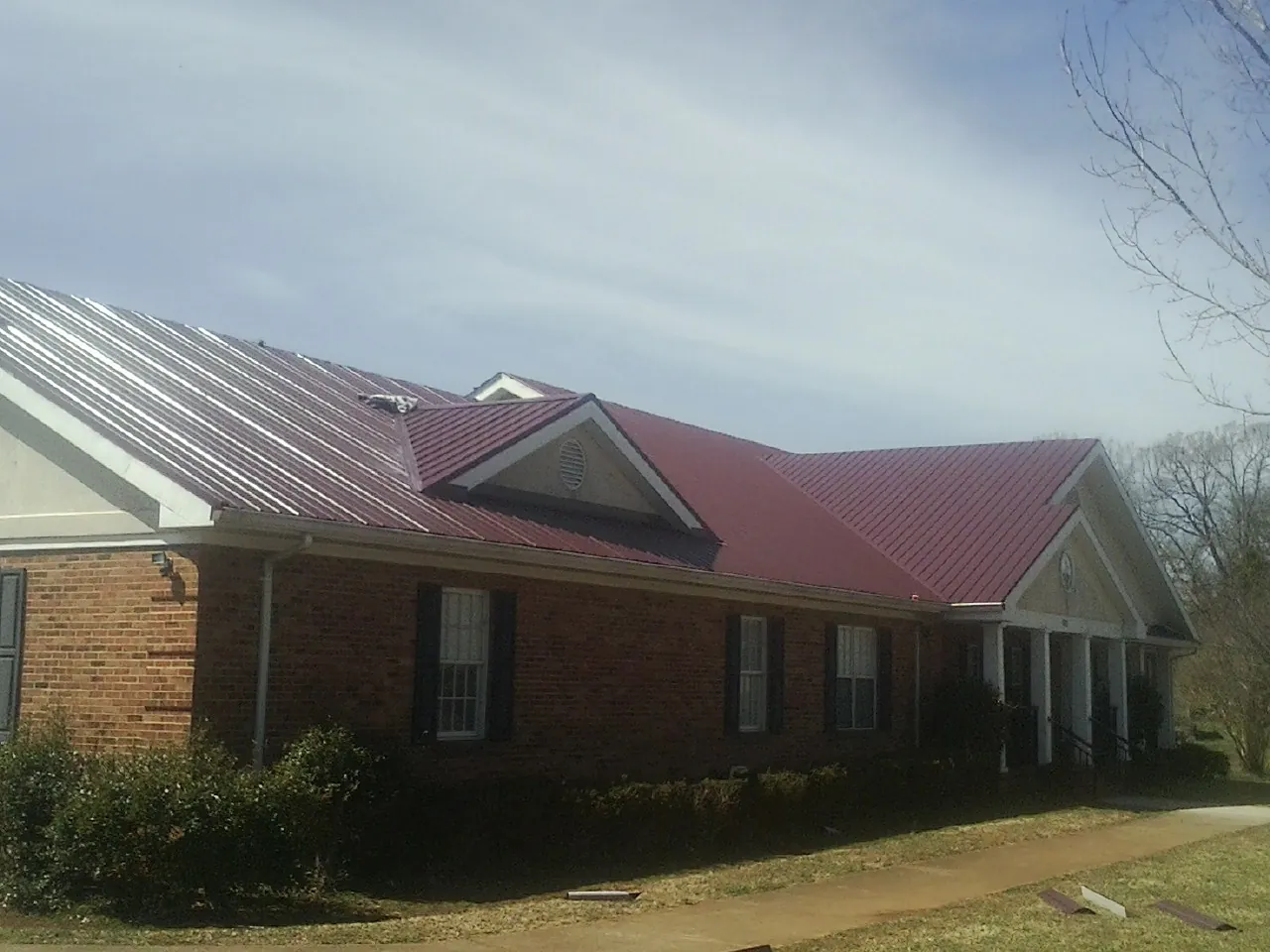Red metal roof with gabled entries on a long brick building, from a Hail Damage Roof Repair job in King Hill