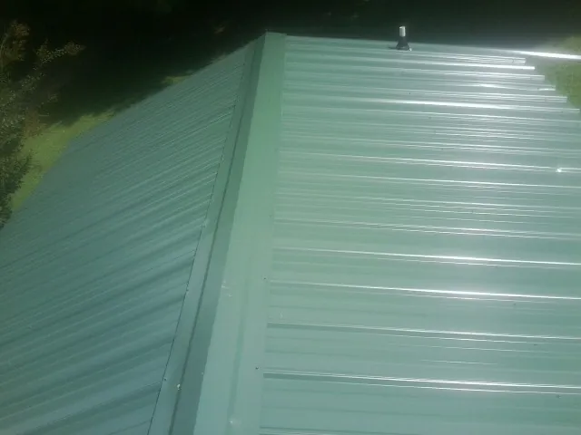 New green metal panels meeting at the ridge of a roof — Flat Roof Repair work by our crew in King Hill