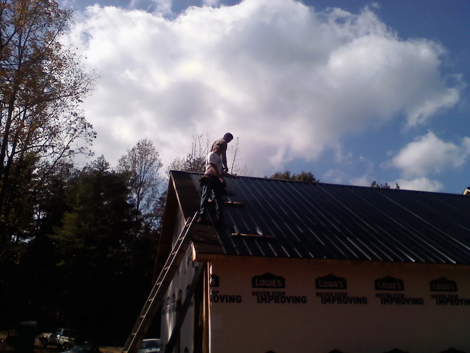 Roofer fastening dark metal panels high against a cloudy sky, from a Roof Inspection job in King Hill