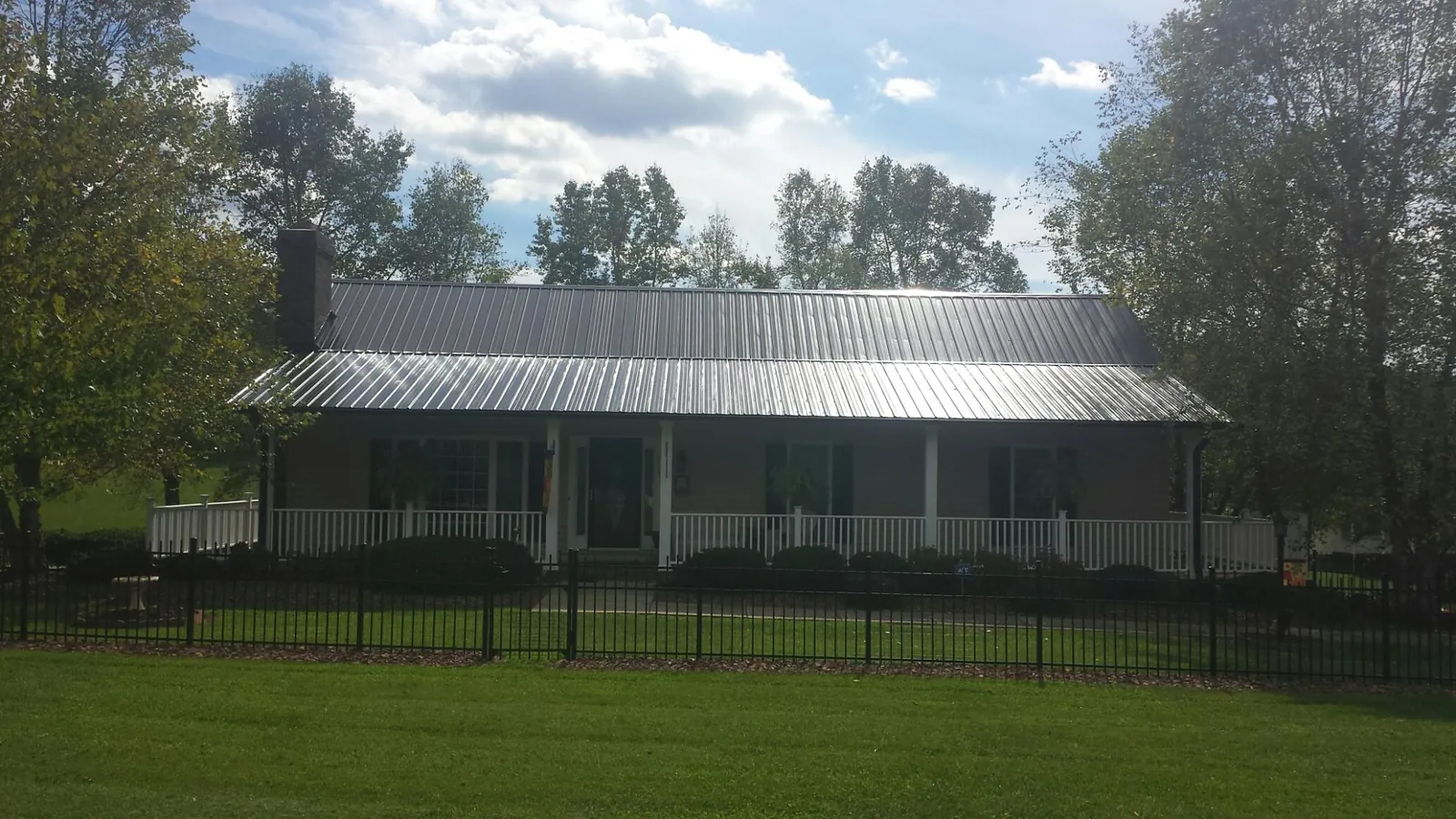 Gray metal roof on a brick ranch with a full width front porch — Gutter Guard Installation work by our crew in King Hill