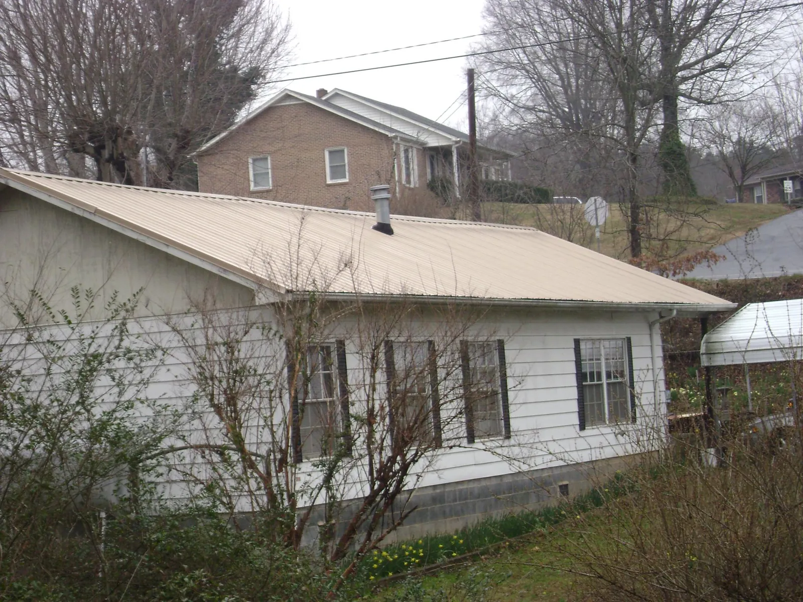 Tan metal roof on a white sided house set into a hillside — Commercial Roofing by Roofing Brothers in King Hill