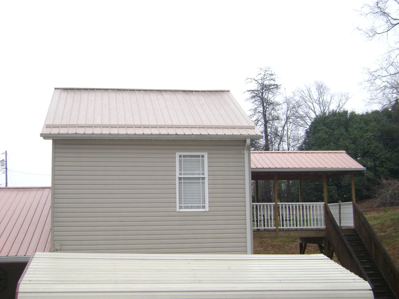 Tan metal roofs on a two story addition and attached porch, from a Roof Replacement job in King Hill